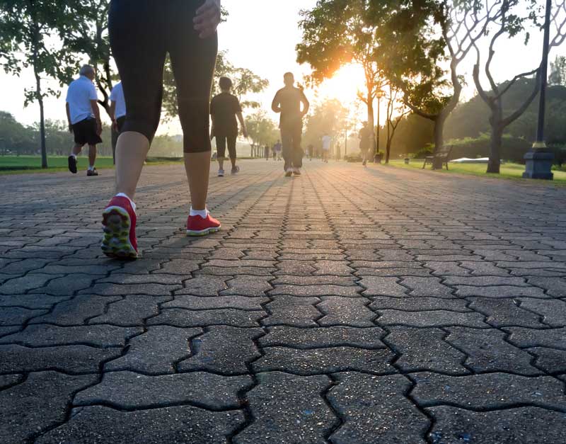 A person walks on a brick-paved path at a park during sunrise, with other walkers in the distance - Podiatrist Visalia