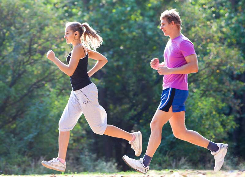 A man and woman jog together on a trail surrounded by greenery, with the woman wearing headphones - Podiatrist Visalia
